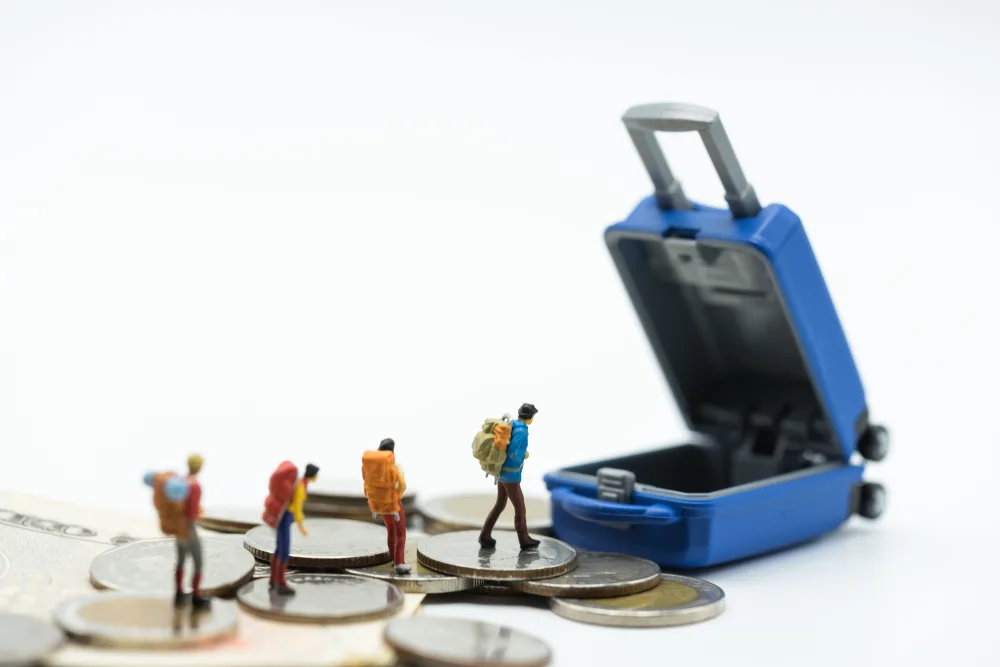 Concept showing how much does travel insurance cost with miniature people walking on coins to suitcase