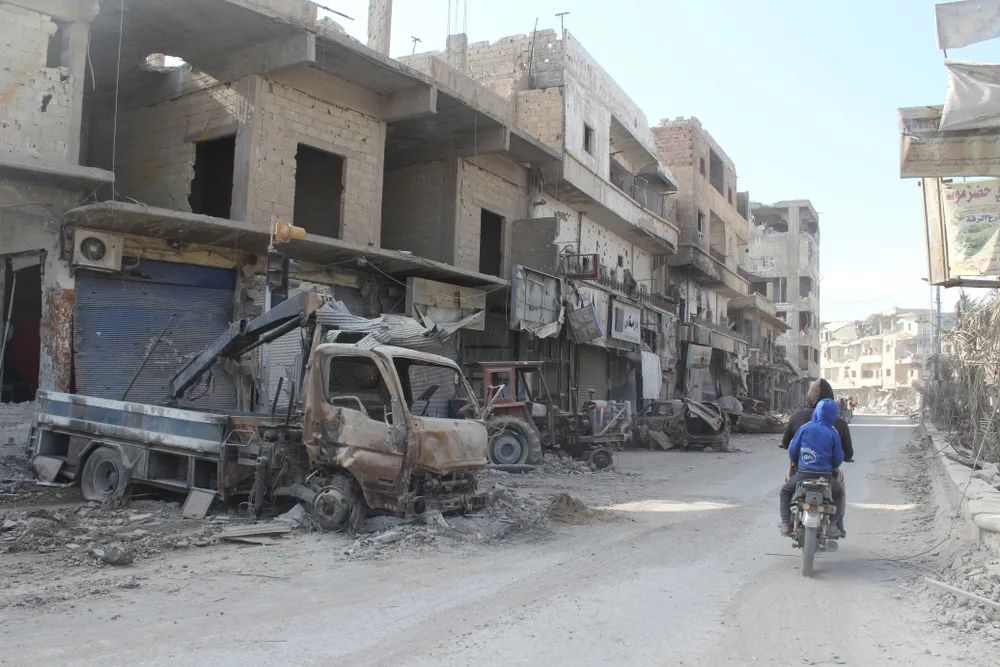 Al-Rakka pictured from the POV of a walker with shelled-out buildings and burned trucks lining the street
