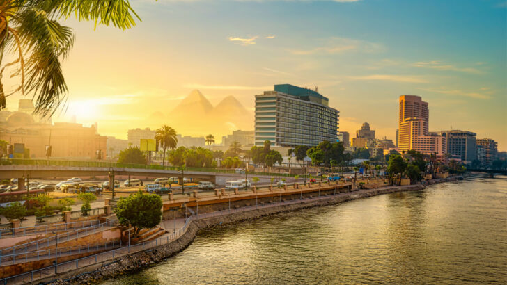 Image of the downtown city pictured from across the Nile at dusk with the pyramids in the background for a piece titled Is Cairo Safe to Visit