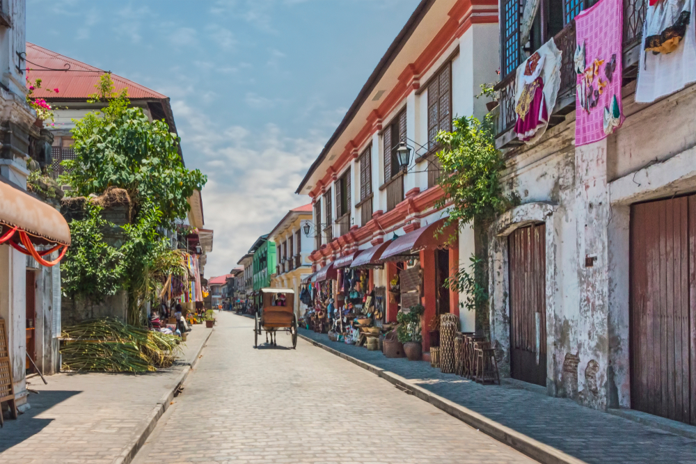 Idyllic town with stone homes and vines running up the old colonial-style homes with a horse-drawn carriage pulling a man down a street for a piece on whether the Philippines are safe to visit