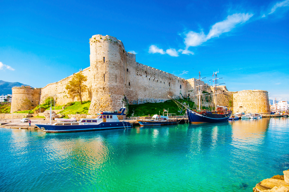Kyrenia Castle as seen from a boat with teal water reflecting the structure on a blue sky day