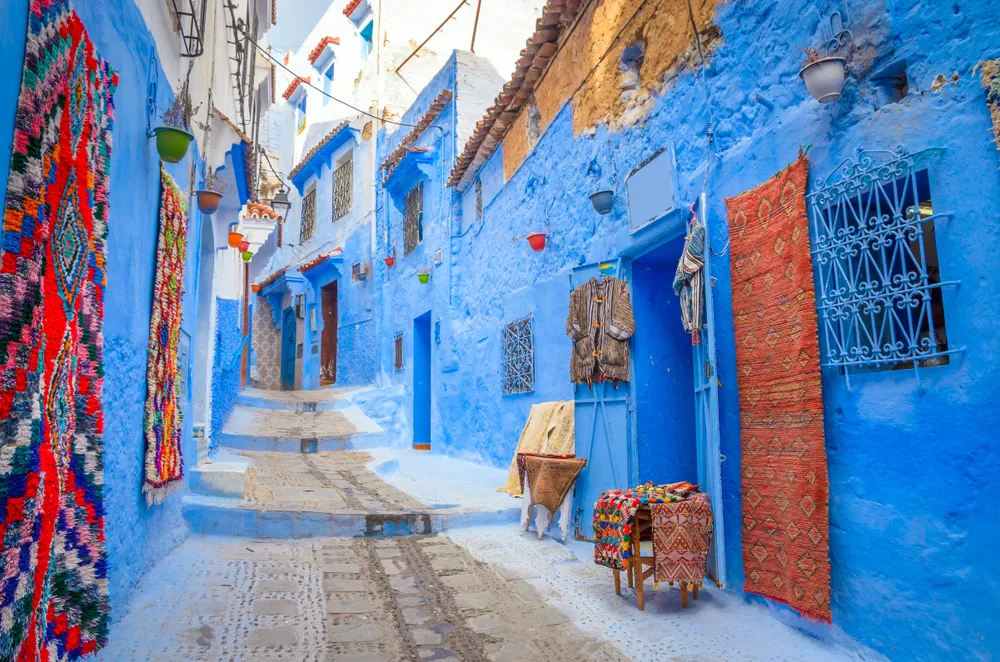 The neat blue walls of Chefchaouen, one of our top picks for where to visit in Morocco, pictured from the street with tapestries hanging from the walls