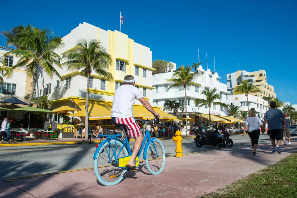 View from a sidewalk on Ocean Drive pictured with people walking and biking down the street