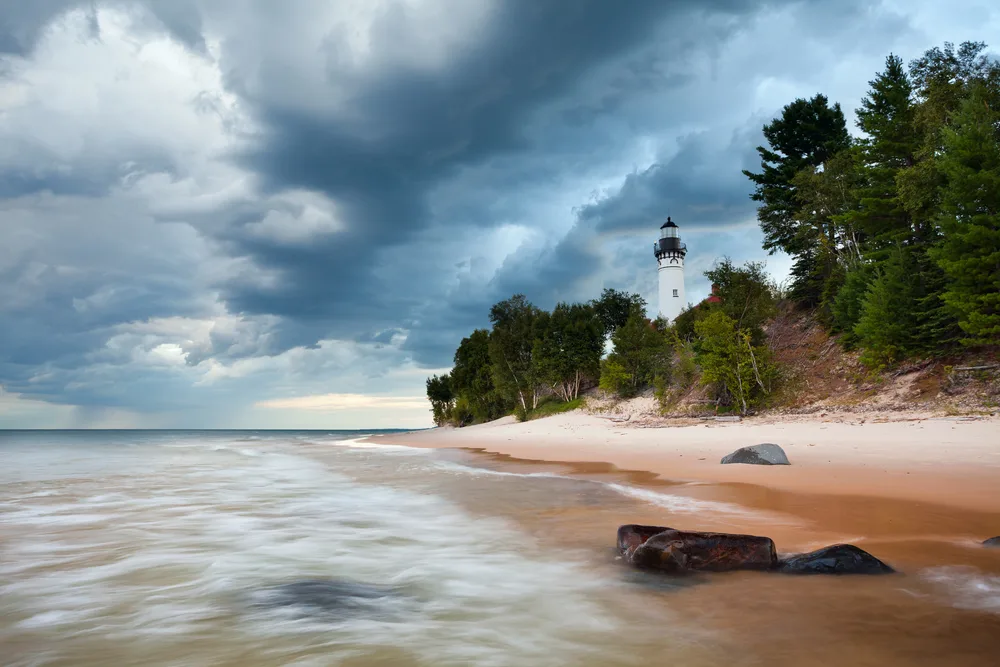 White lighthouse on the edge of a white sand beach in Pictured Rocks with semi-cloudy skies overhead