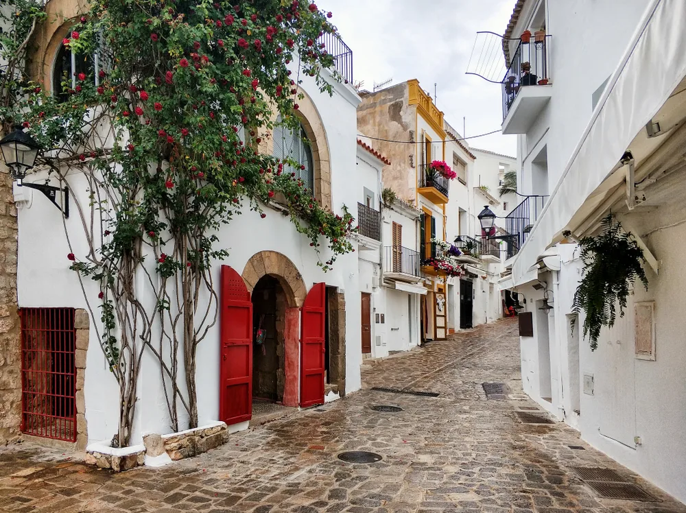 Empty street pictured during the least busy time to visit Ibiza with white buildings and red doors along either side of the stone street