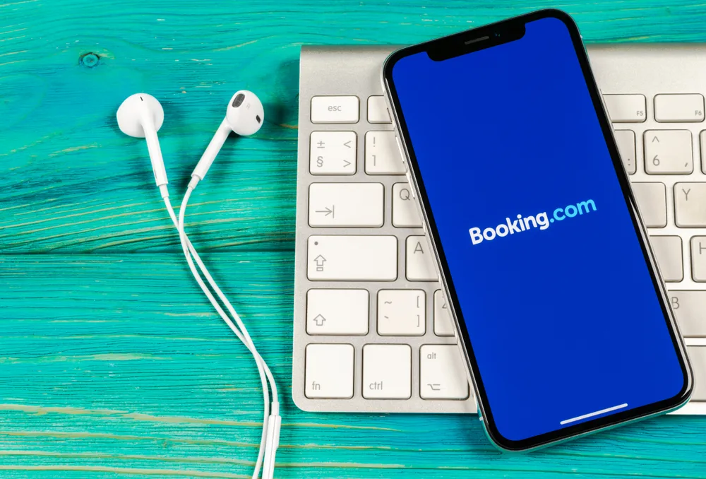Booking.com app on iPhone X resting on a white keyboard with headphones nearby for a piece on the best hotel booking sites to use