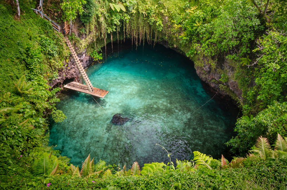 Stairs leading down to a diving platform in the Sua Trench pictured from above with trees surrounding the watering hole during the least busy time to visit Samoa