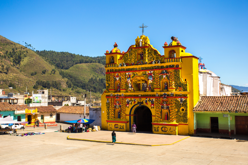 Yellow church in San Andres Xecul on a clear day with a single man praying in front of it