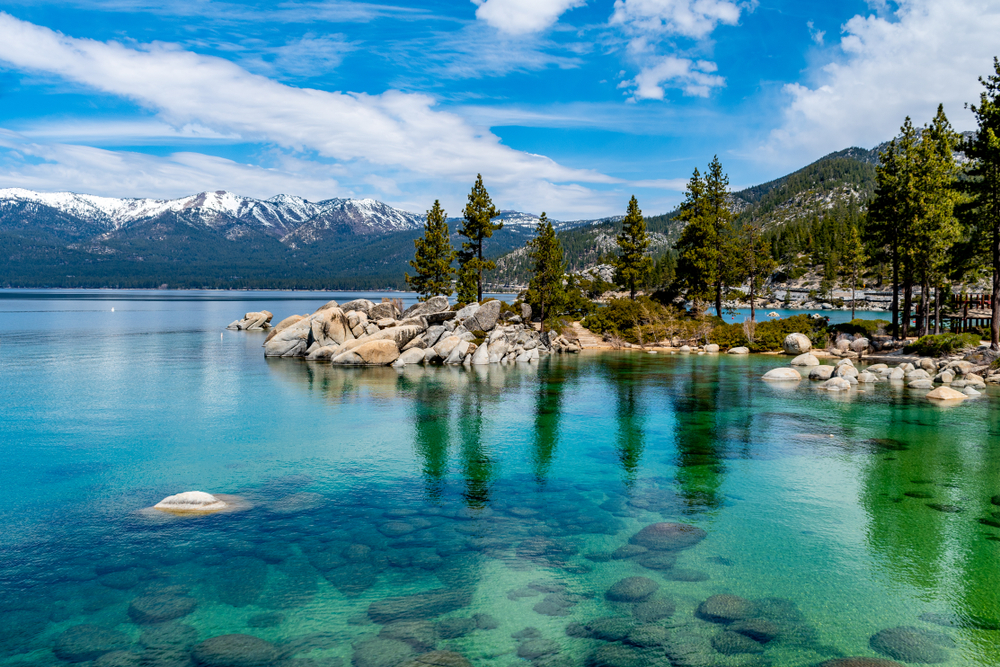 Spring view of Lake Tahoe, one of the best places to visit in April, pictured on a clear day with still lake water seen by the rocks