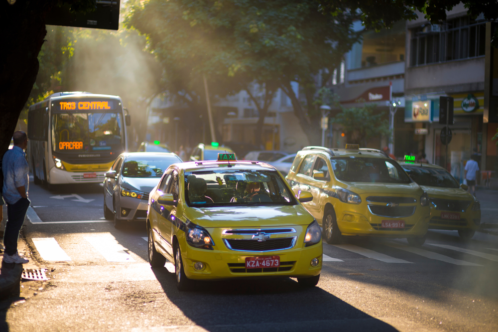 Yellow taxi cabs in Rio pictured on a hazy day with light beaming down on them through the trees