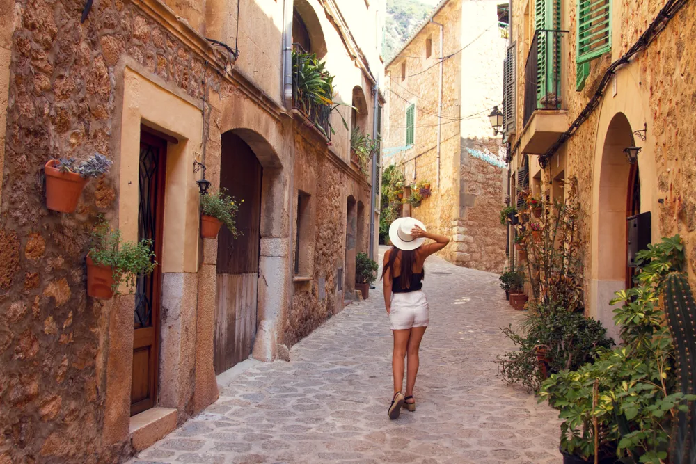 Cute woman in white shorts pictured with a flat-brimmed hat on looking upward during the least busy time to visit Mallorca 