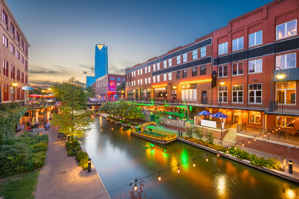View of buildings on either side of a canal in Oklahoma City, one of the best places to visit in July, as seen at dusk with a still sky