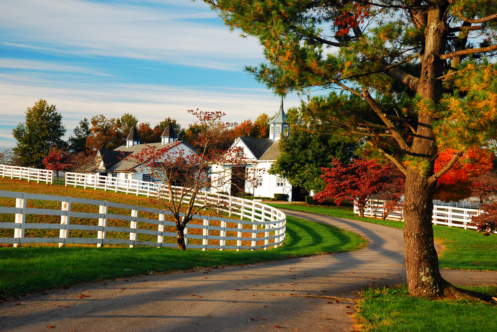 Winding dirt road leading to a white barn in the countryside pictured during the best time to visit Kentucky