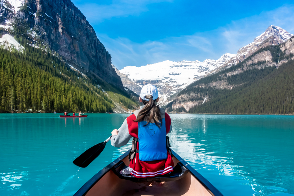 Asian woman in the front of a canoe rowing her oar in the teal water in the summer, the overall best time to visit Lake Louise