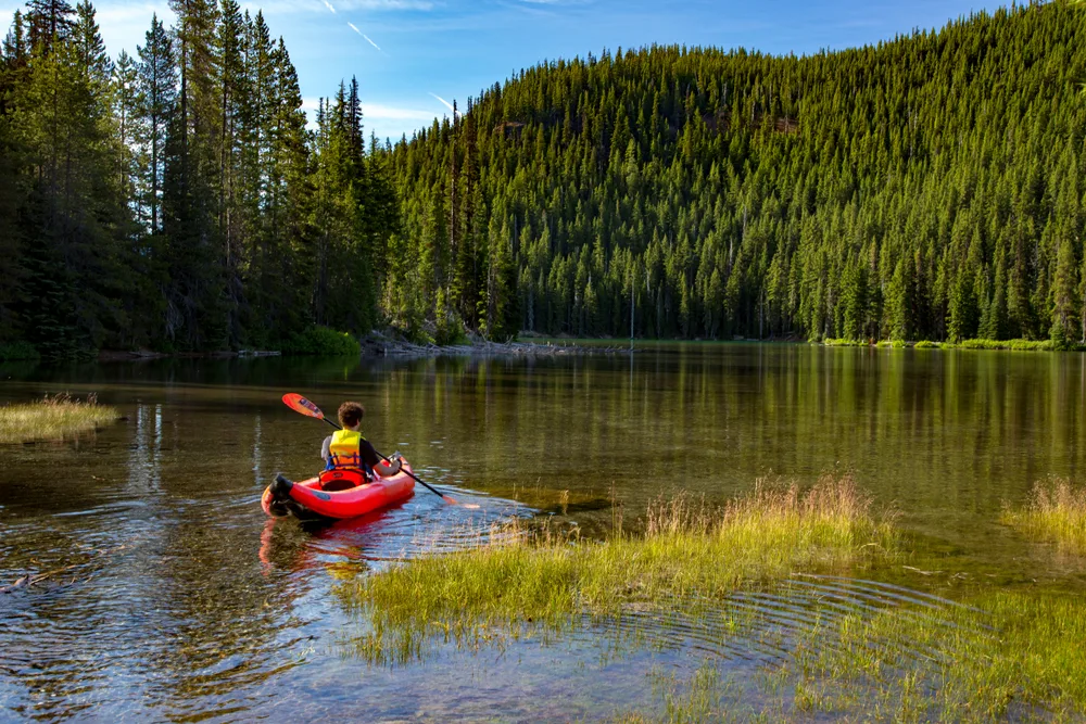 Young man in an inflatable canoe floating on the water in the middle of a lake in Bend Oregon during the least busy time to visit