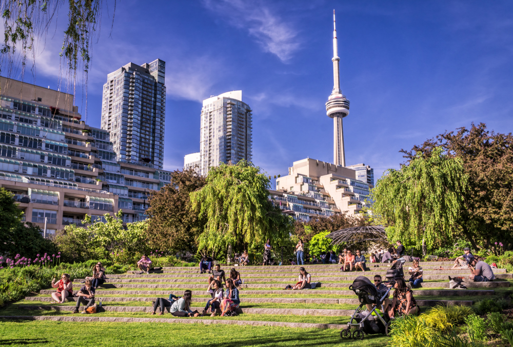 Lovely day in Toronto, one of the best places to visit in July, pictured on a blue-sky day with people in a park lounging and soaking up the nice weather