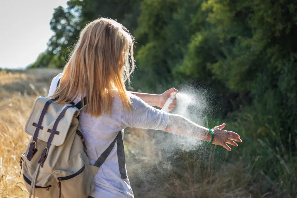 Woman sprays insect repellent on her skin and clothing to prevent mosquito borne diseases for a piece on vaccines needed to travel to Africa