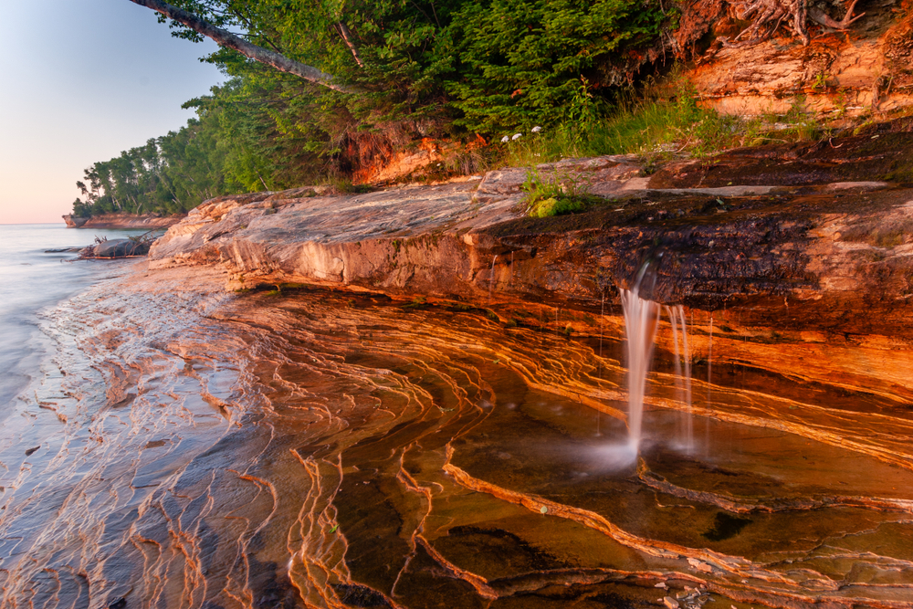 Pictured rocks on the coastline that are red in color with a waterfall in the middle during the best time to visit the park