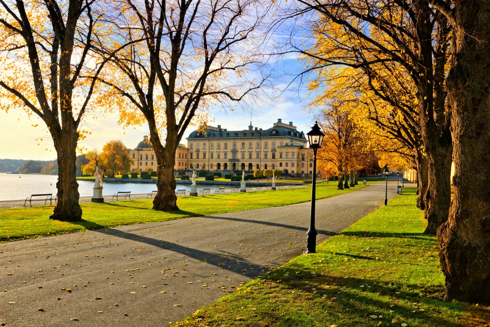 Idyllic view of Drottningholm Palace as seen through a row of trees along a walking path in Stockholm, one of the best places to visit in Sweden