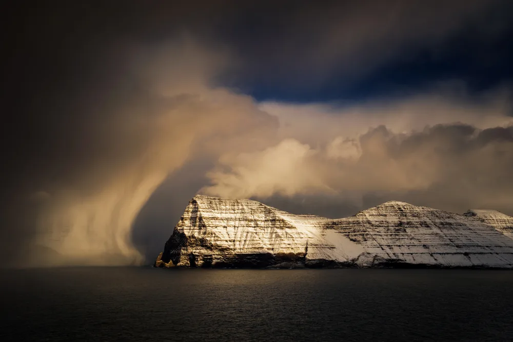 Snowstorm rolling in over the coastline with snow falling on the rocks during the worst time to visit the Faroe Islands