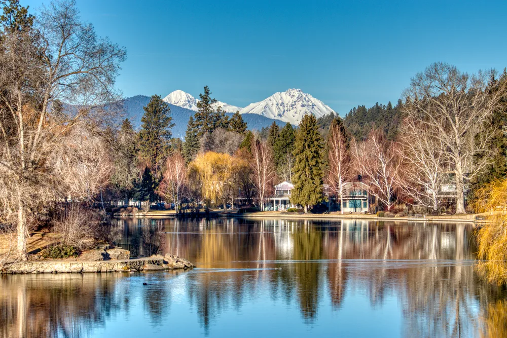View of Mirror Pond from the side of the lake looking out toward the mountains pictured during the winter, the worst time to visit Bend, Oregon