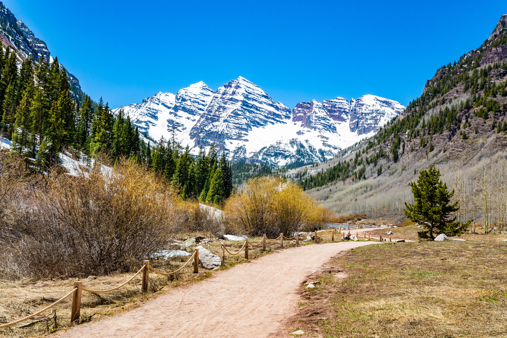 Gorgeous winter day pictured during the least busy time to visit Maroon Bells with snow-capped mountains in the background and a dirt path in the foreground
