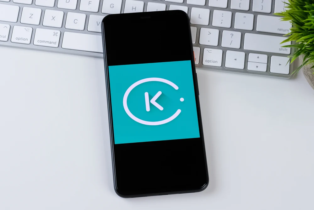 Kiwi.com turquoise logo on a smartphone screen lying on a white keyboard for a piece on the best websites to book flights