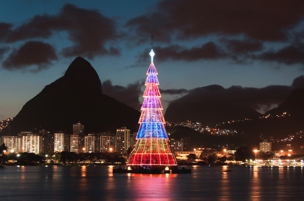 Night view of the bay and towering mountains in the background with a Christmas trees in the middle of the water pictured as one of the best places to visit in December