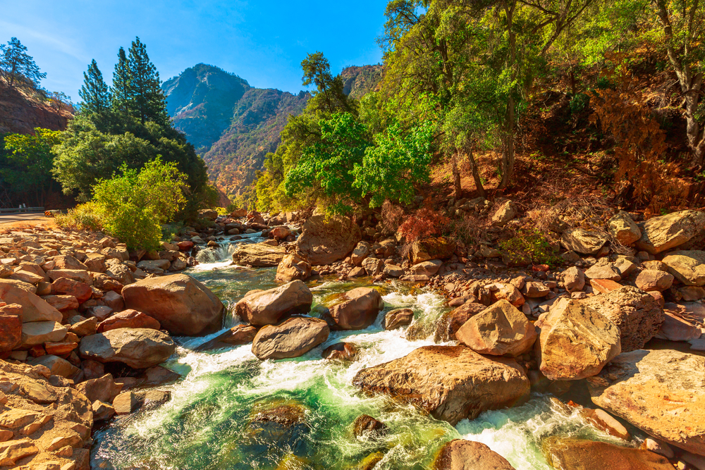 Gorgeous view of the least busy time to visit Kings Canyon National Park with a stream flowing down the rocky valley with a wooded mountain in the background