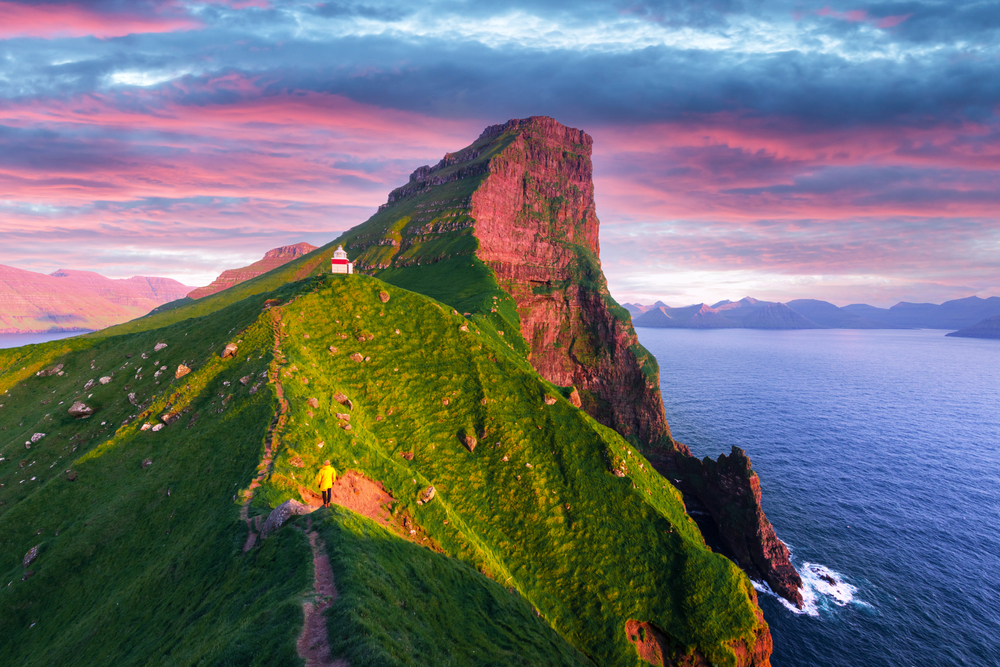 Man hiking up to the Kallur Lighthouse with green hills on either side of the path during the best overall best time to visit the Faroe Islands