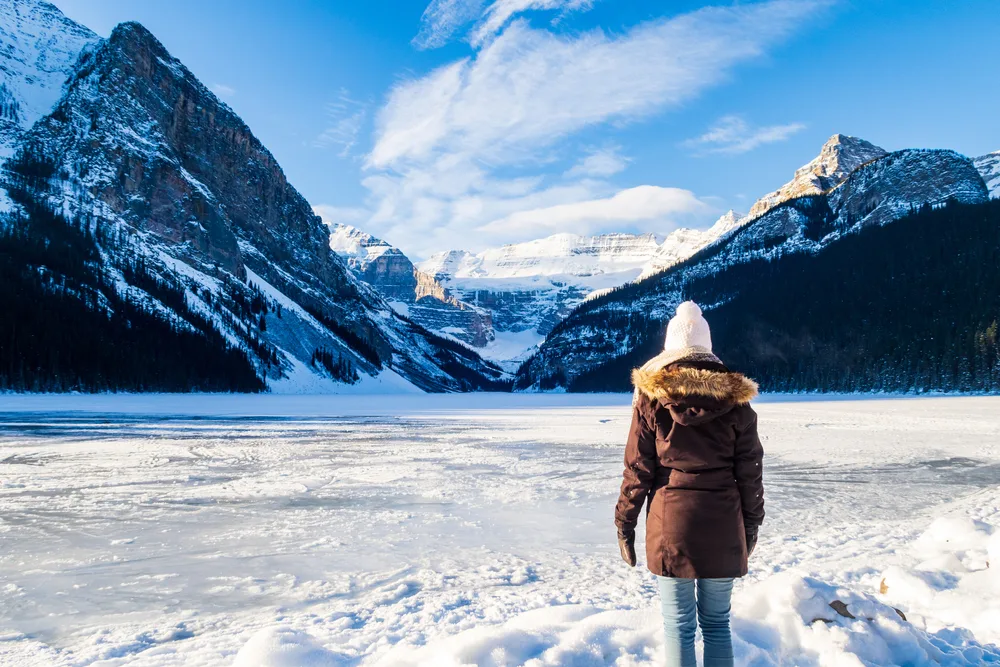 Back view of a woman looking toward a frozen Lake Louise while wearing a puffy coat