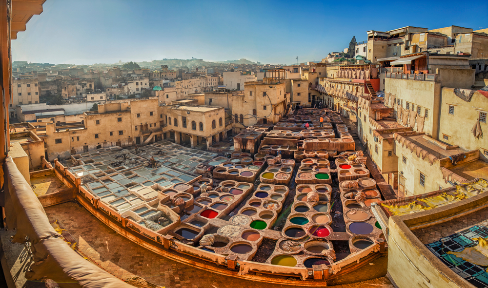 Panoramic view of the colorful tannery in Fez, one of the best places to visit in Morocco, pictured from a balcony with towering buildings overlooking it