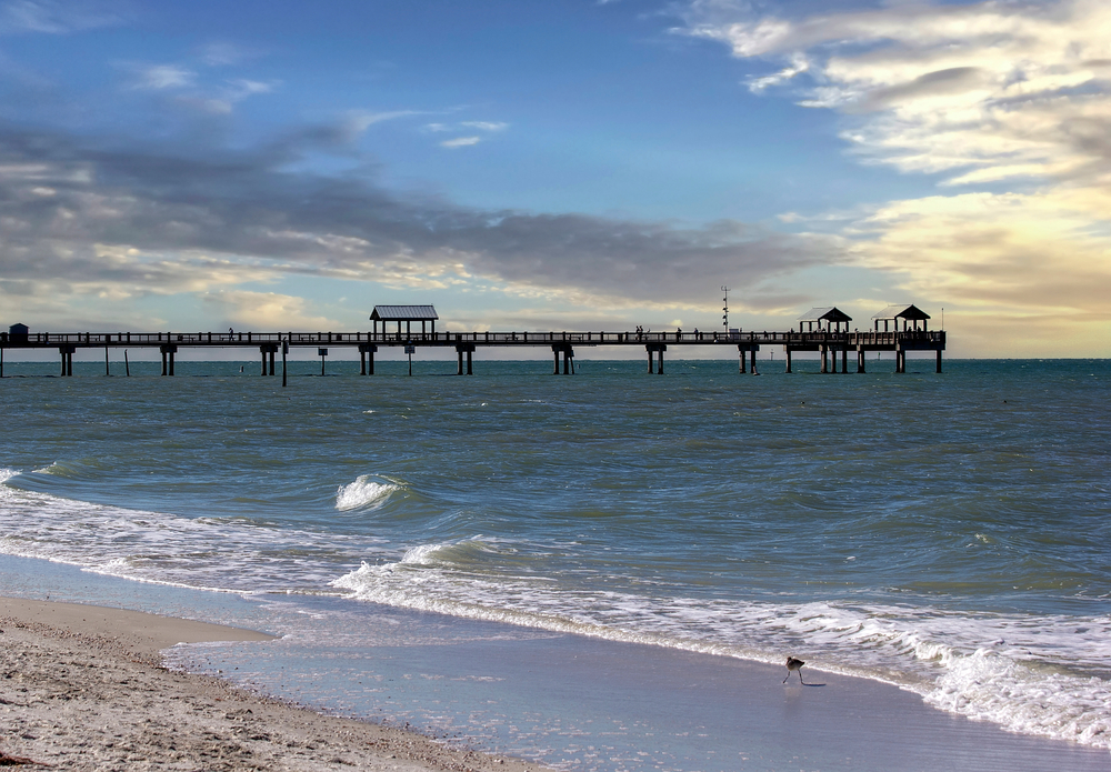 View of Pier 60 in the distance at dusk with clouds in the skies as waves lap the shores during the best time to visit Clearwater Florida