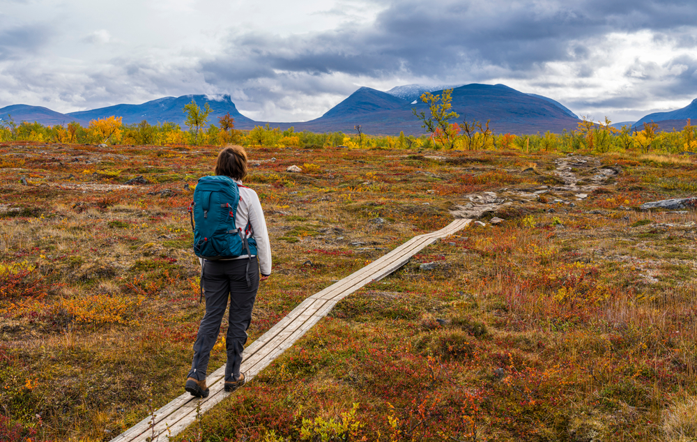 Woman with a blue backpack walking on a small wooden path in Abisko, one of the best places to visit in Sweden