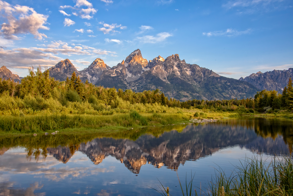 Schwabacher's Landing in Jackson Hole, one of the best places to visit in May, as seen from the edge of a pond with mountains rising high into the air