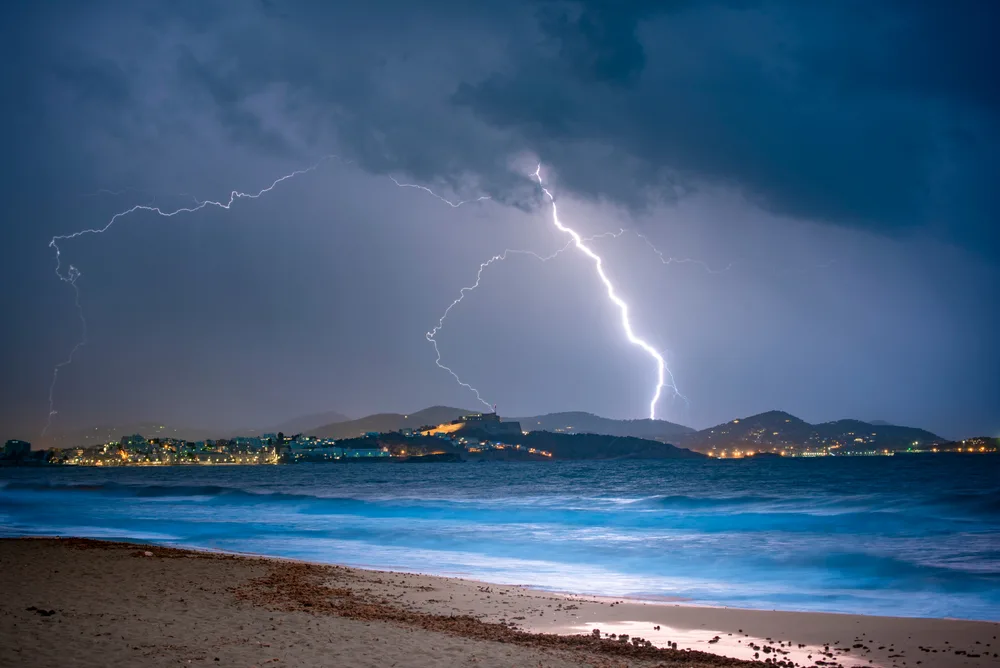 Lightning striking a mountain in Ibiza with dark clouds and rain overhead pictured during the worst time to visit Ibiza