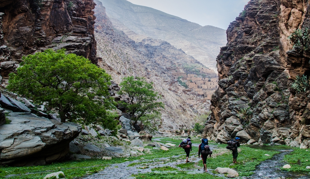 Three tourists with backpacks hiking up a rocky and wet path between huge rock faces in the High Atlas for a piece on the best hiking backpacks