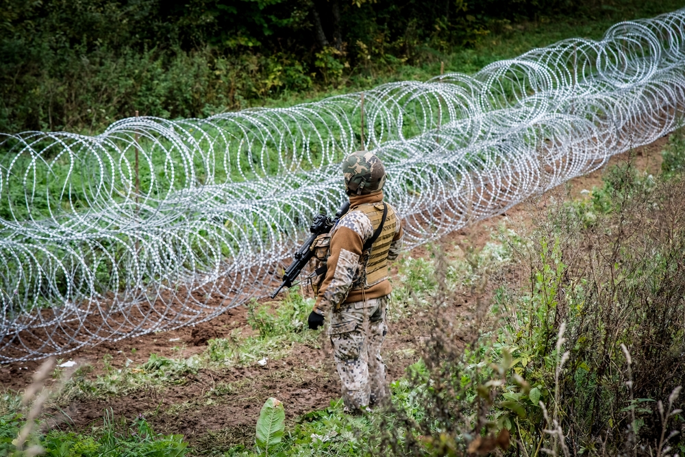 Guard stands at the border of Latvia and Belarus with barbed wire in front of him