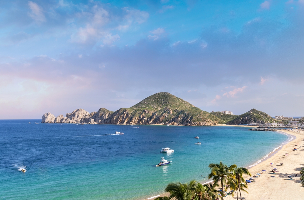 Picturesque view of the beach in Cabo San Lucas featuring a big rock and white sand beaches with teal water next to it