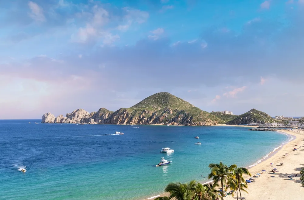 Picturesque view of the beach in Cabo San Lucas featuring a big rock and white sand beaches with teal water next to it