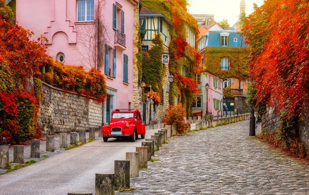 Cozy street in Montmartre in Paris, one of the best places to visit in September, seen in autumn with an old red car driving down the stone path