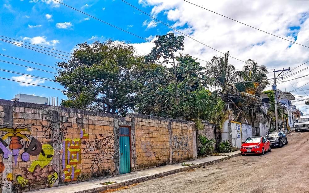Photo of red and black cars on a dirt road next to graffiti in Playa del Carmen for a guide to whether or not it's safe to visit