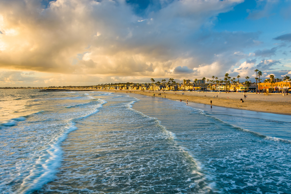 Sun setting over the coast of Newport Beach, one of the best places to visit in April, as seen from the perspective of a person standing in the water