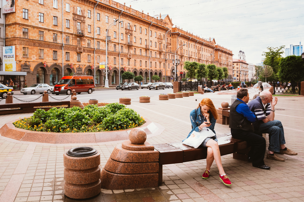 Pretty and fair-skinned redhead on a bench next to two men in a historical part of Belarus