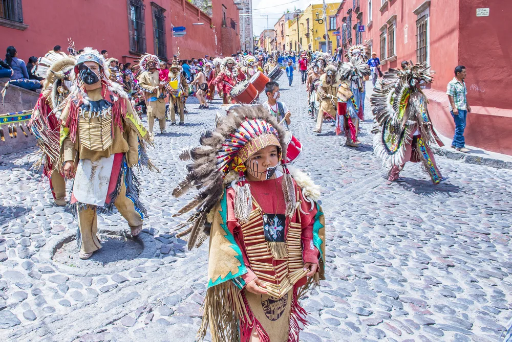 Young and old people in Native American costumes participating in a walk for the Festival of Valle del Maiz during the best time to visit San Miguel de Allende