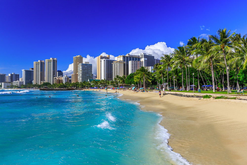 Waikiki beach with blue skies pictured with waves lapping the tan sand, listed as one of the best places to visit in December