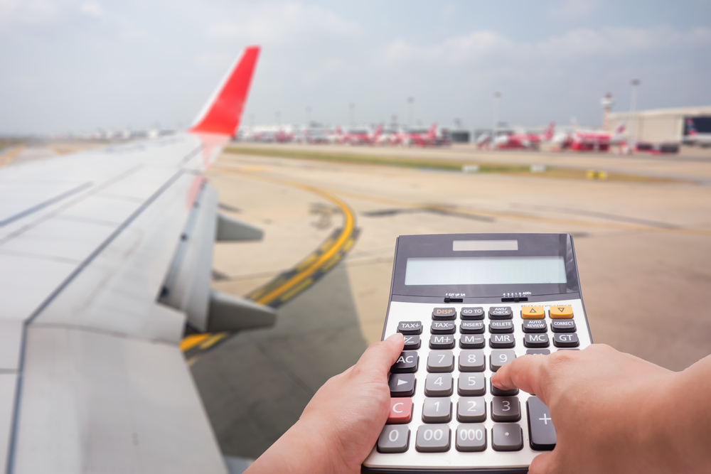 Person holding calculator on airplane runway indicates the concept of how to find cheap flights