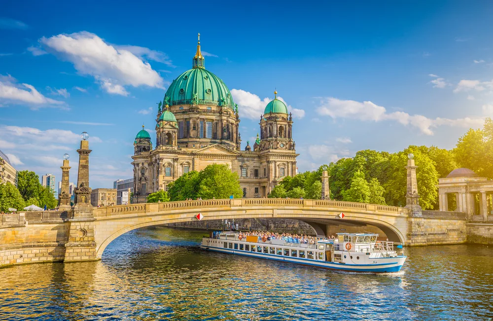 Beautiful sunrise over the cathedral in Berlin, one of the best places to travel to in August, with a boat traveling on the river in the foreground