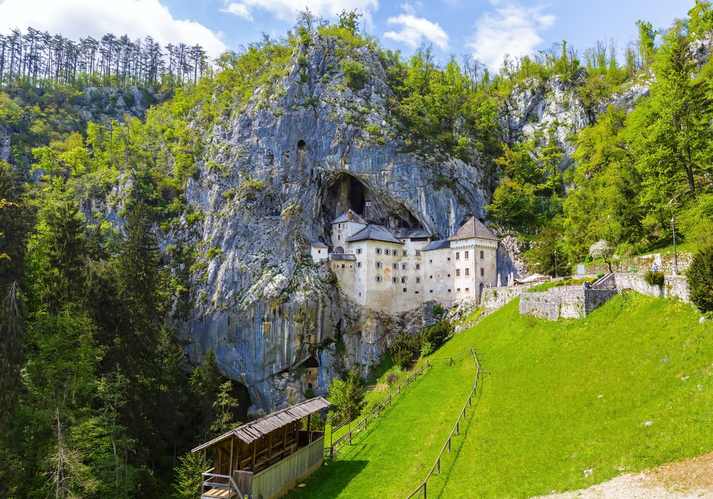 Predjama Castle pictured in the spring, the overall cheapest time to visit Slovenia, pictured with green grass on the hillside beside the castle