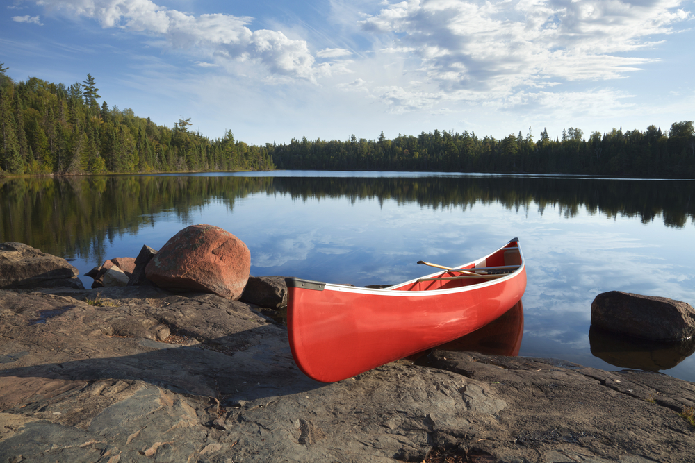 Red canoe sitting partially on the rocks of a lake during the best time to visit Minnesota